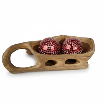 Elongated hand-carved wooden tray with loop handle, open oval cutouts along the base, and two red mosaic decorative balls sitting inside, on a white background