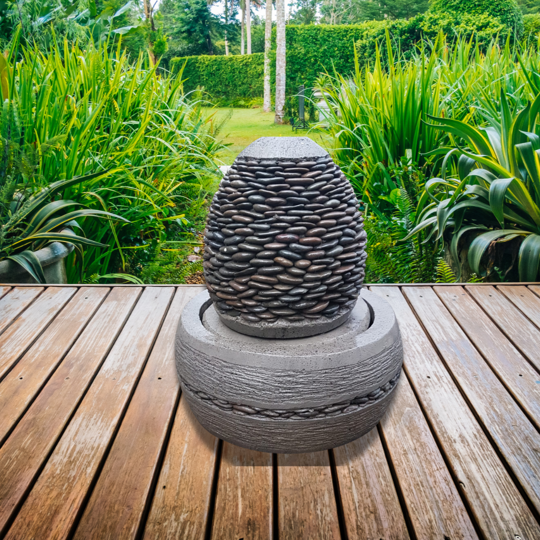 Decorative stone fountain on a wooden deck with greenery in the background