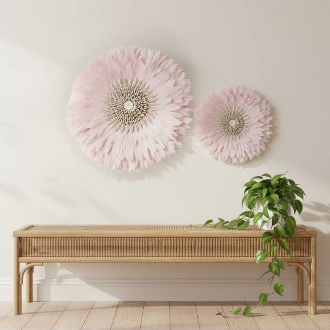 Two pink JUJU hat wall art pieces in 50cm and 35cm grouped together above a rattan bench with a trailing green plant on a warm white wall