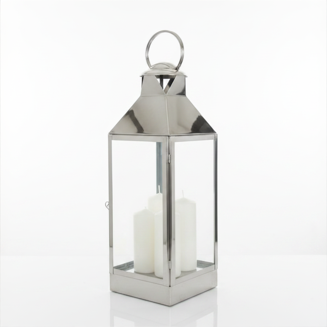 Large polished silver metal lantern with solid pyramid roof, round loop handle, and two white pillar candles, photographed on a white background