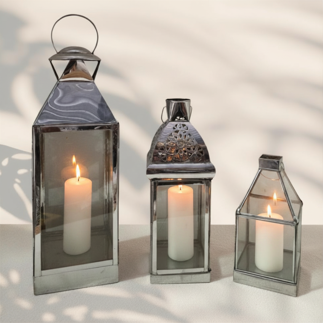 set of three sizes with lit pillar candles casting warm light, styled on a white surface with soft tropical leaf shadows