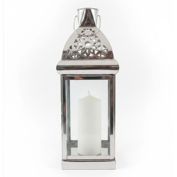 Medium polished silver metal lantern with ornate filigree-cut triangular roof, bucket handle, and single white pillar candle, photographed on a white background