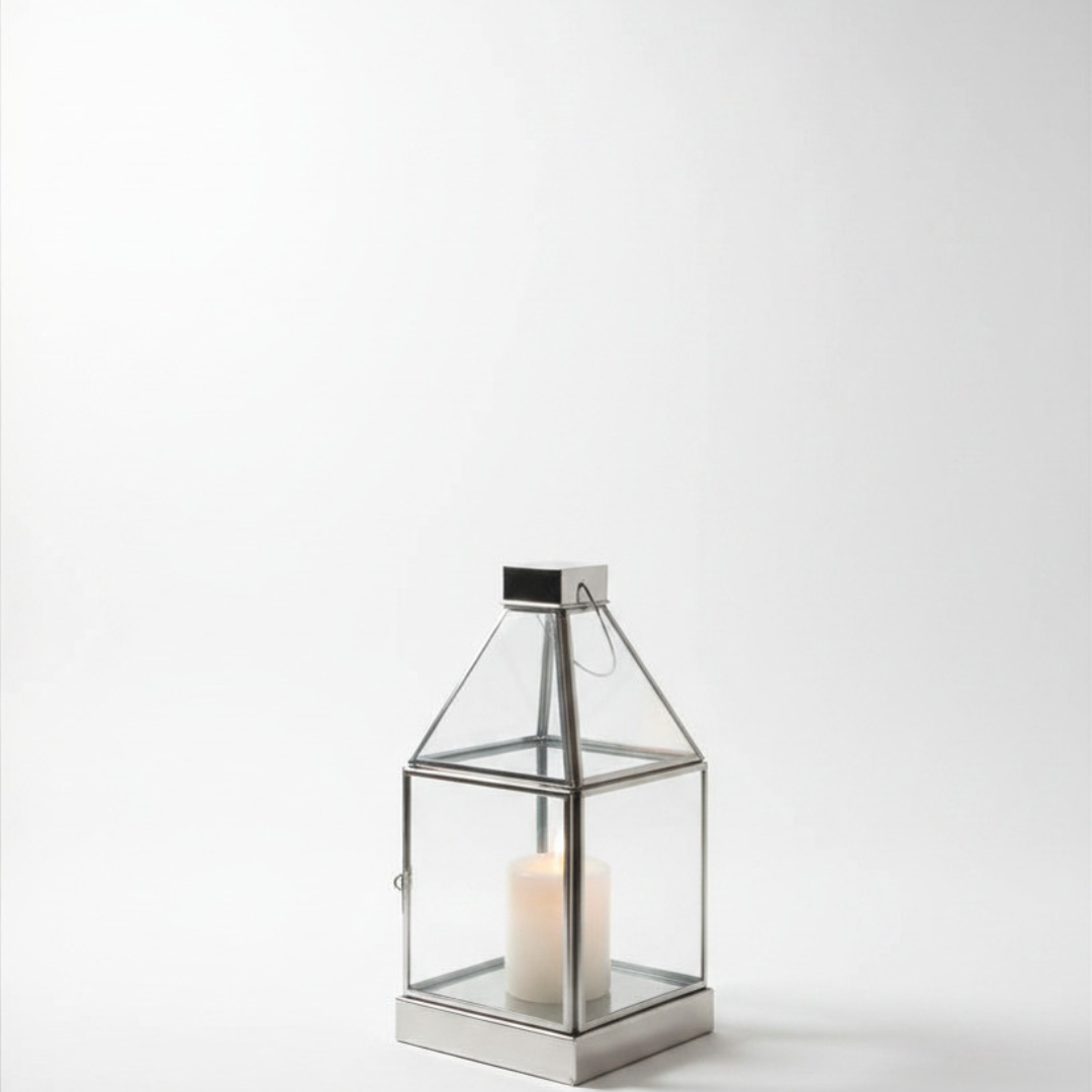 Small polished silver and glass lantern with pyramid roof, wire handle, and single white pillar candle, photographed on a white background