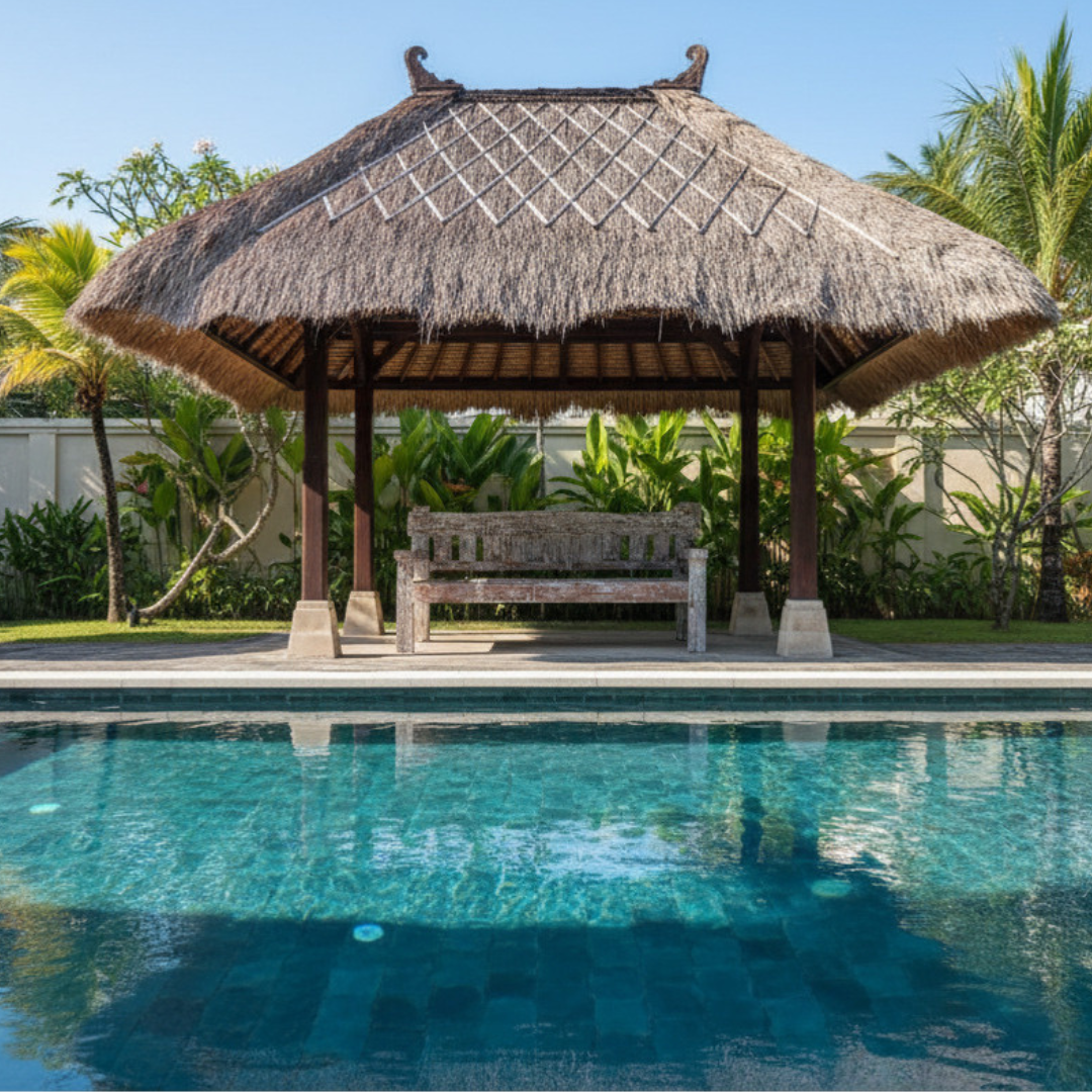 Weathered white-painted timber bench seat under a thatched Balinese hut beside a pool, showing aged grain texture and rustic handcrafted finish with tropical garden in the background