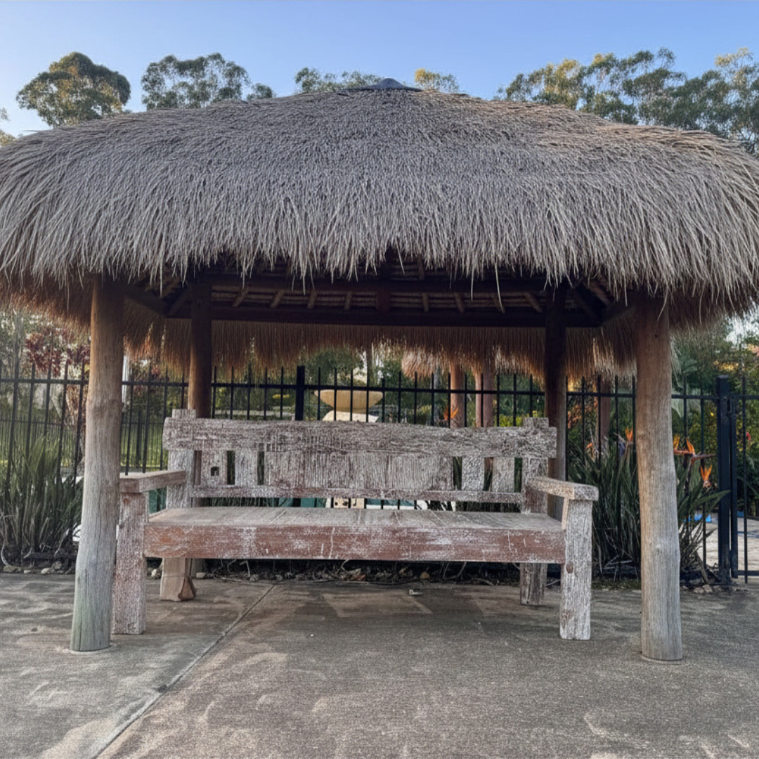 Reclaimed timber day bed furniture under a traditional Balinese pavilion with ornate roof, tropical garden and pool in the foreground