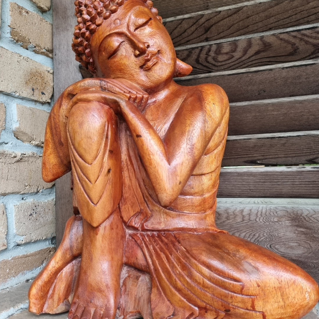 Close-up of a hand-carved wooden Buddha statue displayed on a brick shelf