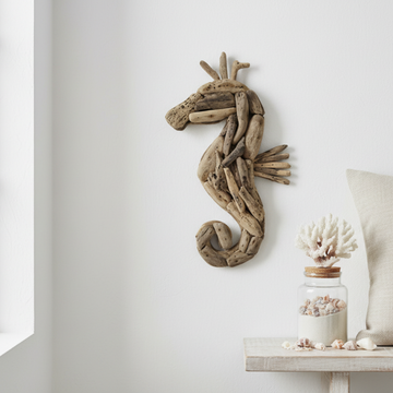 50CM A seahorse-shaped wall decor piece made from natural driftwood, mounted on a white wall above a small shelf with seashells and a glass jar.