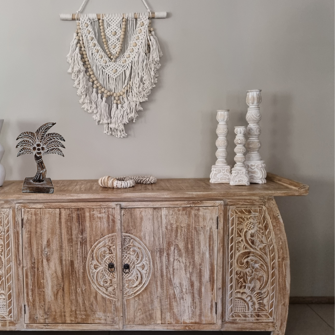 Wooden sideboard with decorative items against a gray wall with a wooden coco tree wooden candle holder shell decor boho wall art 