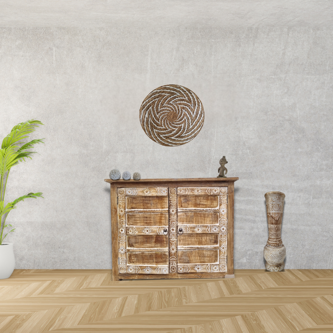 Seagrass spiral wall art on grey concrete wall above carved timber cabinet with palm plant and tribal vase – boho living room wall décor Australia