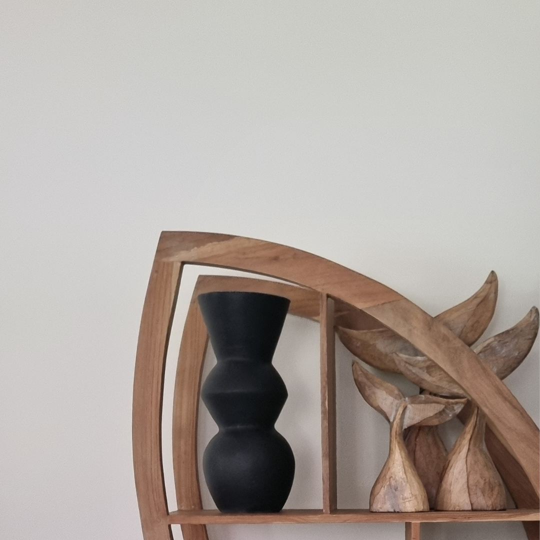 Dark decorative object displayed on a wooden shelf with natural timber decor pieces
