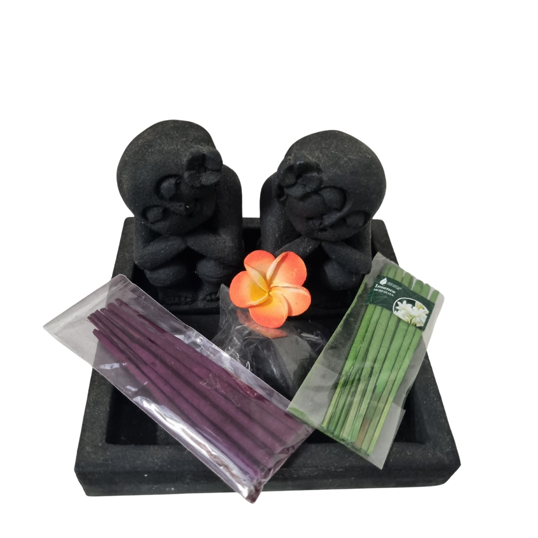 A round incense holder featuring a stone-carved figure with incense sticks placed on top, surrounded by decorative stones and two types of sand.
