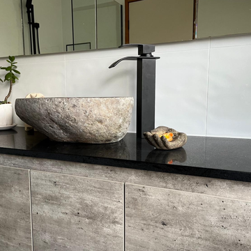 Natural river-stone basin with a rough grey exterior, black waterfall tap and potted greenery on a dark countertop