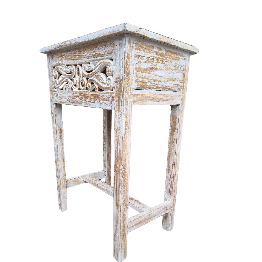 White wash wooden Balinese table with deep, raised carvings, placed against a plain white wall for strong contrast.