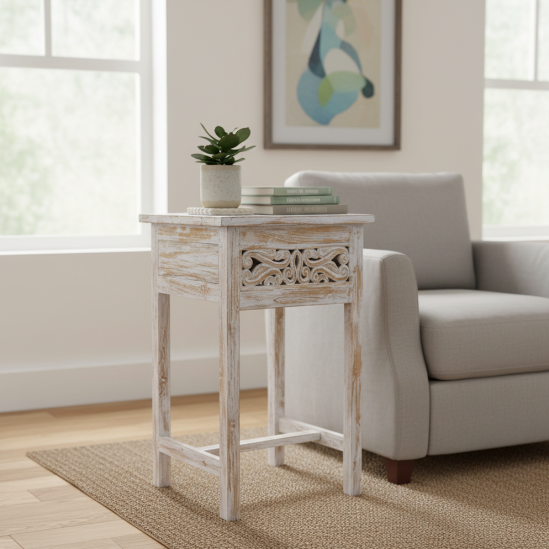 White distressed side table with a plant and books next to a gray sofa in a living room.