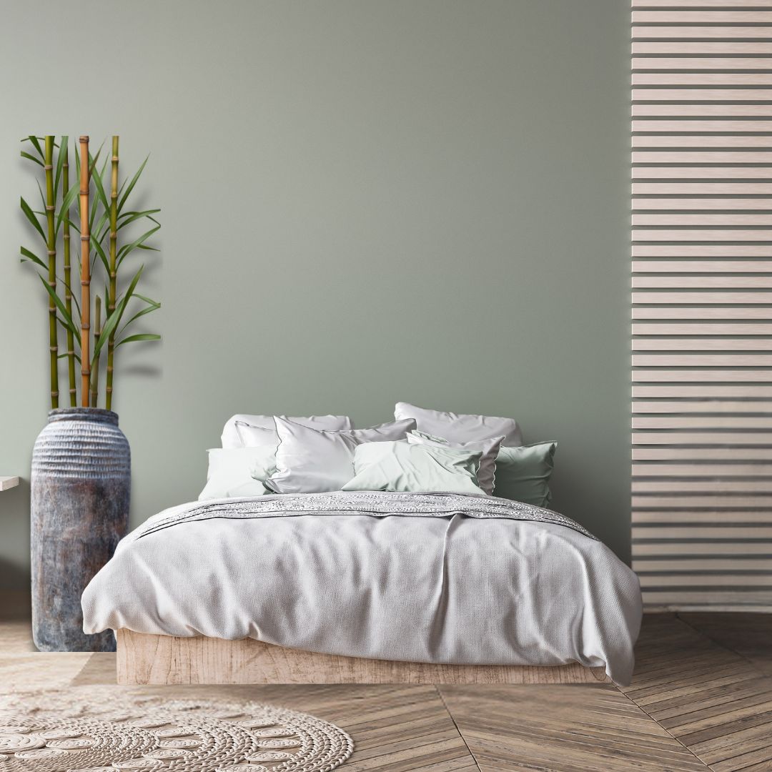 Neatly made bed with gray bedding in a room with a plant and striped wall.