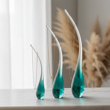 Three teardrop glass jewellery holders in small, medium and large with gold chain necklaces draped over the stems