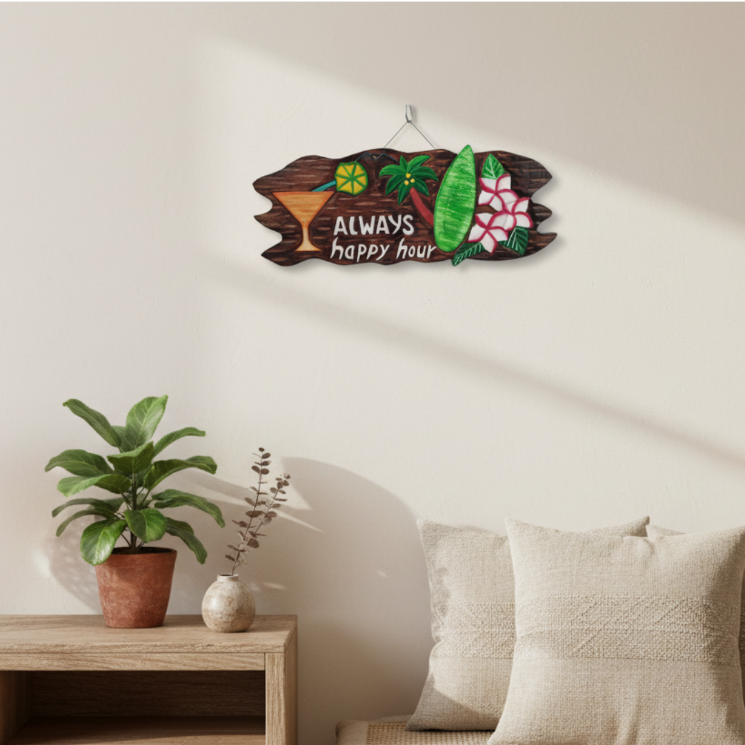 A decorative wooden wall sign with tropical cocktail and surfboard illustrations and the words 'Always Happy Hour,' hanging on a beige wall above a side table with a plant and pillows.