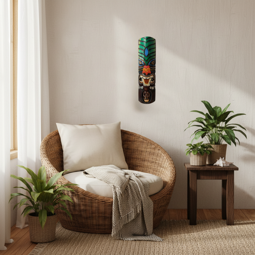 Dark brown carved decoration with tall green feathered headdress, red and orange flower nose, snarling mouth and skull carving at the base, styled in a tropical coastal interior