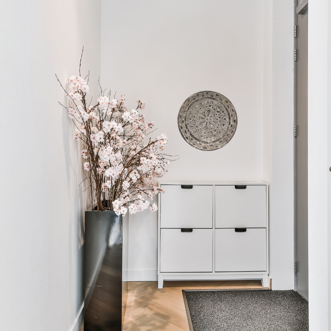 Modern interior with a vase of flowers, white cabinet, and decorative wall plate.