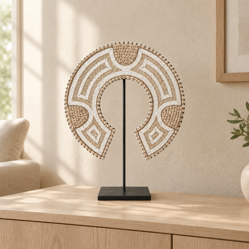 Crescent-shaped ornament with beige and white beadwork on a black metal stand against a neutral background