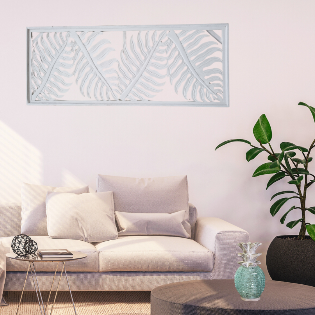 Tropical fern leaf wall hanging in white wash finish displayed horizontally above a sofa in a bright coastal living room with indoor plant