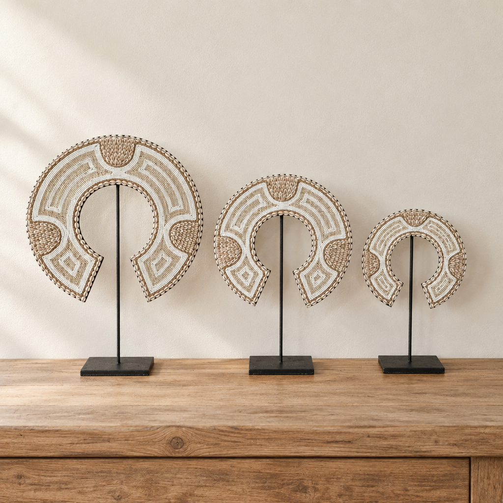 Three crescent-shaped shell and bead decorations in different sizes on black metal stands, displayed on a timber console