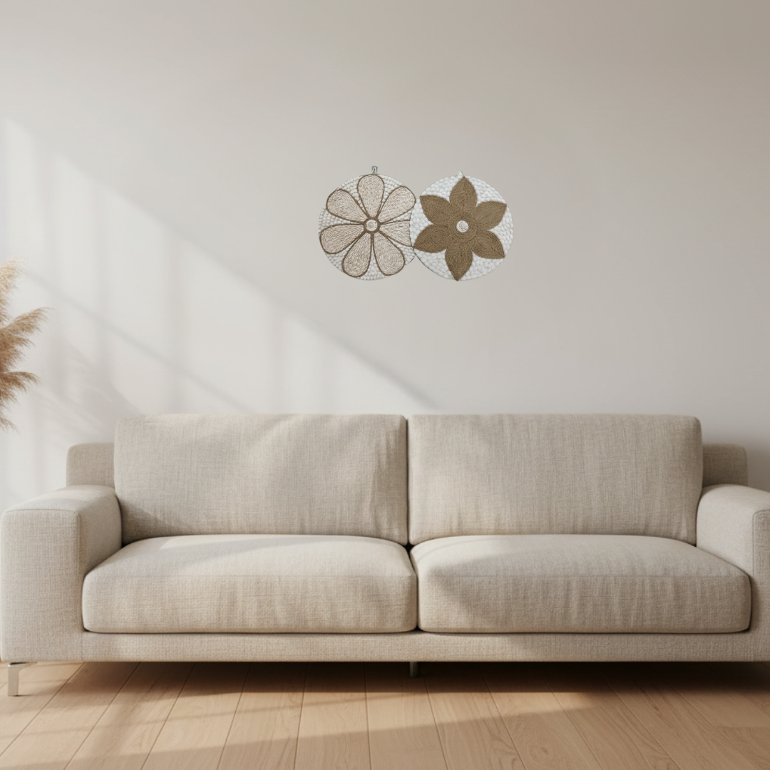 Two small round shell and jute wall art pieces hung above a cream linen sofa in a minimal living room with light timber flooring and dried pampas grass in the corner.