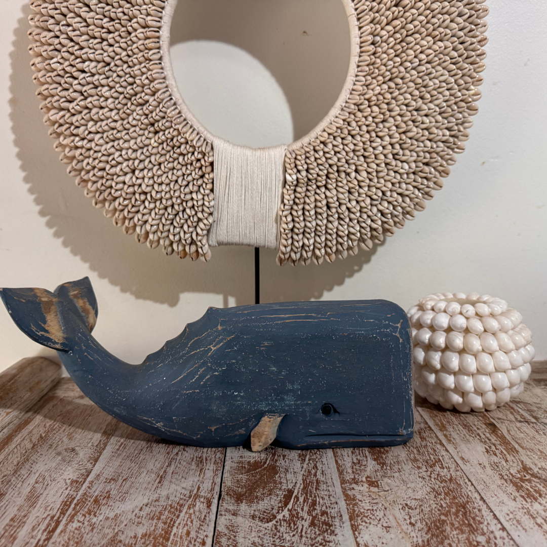 Decorative wooden whale on a wooden surface with a textured wall and spherical object in the background.