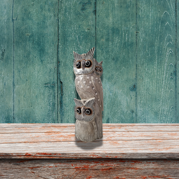 Decorative owl sculpture on a wooden surface with a teal wooden panel background