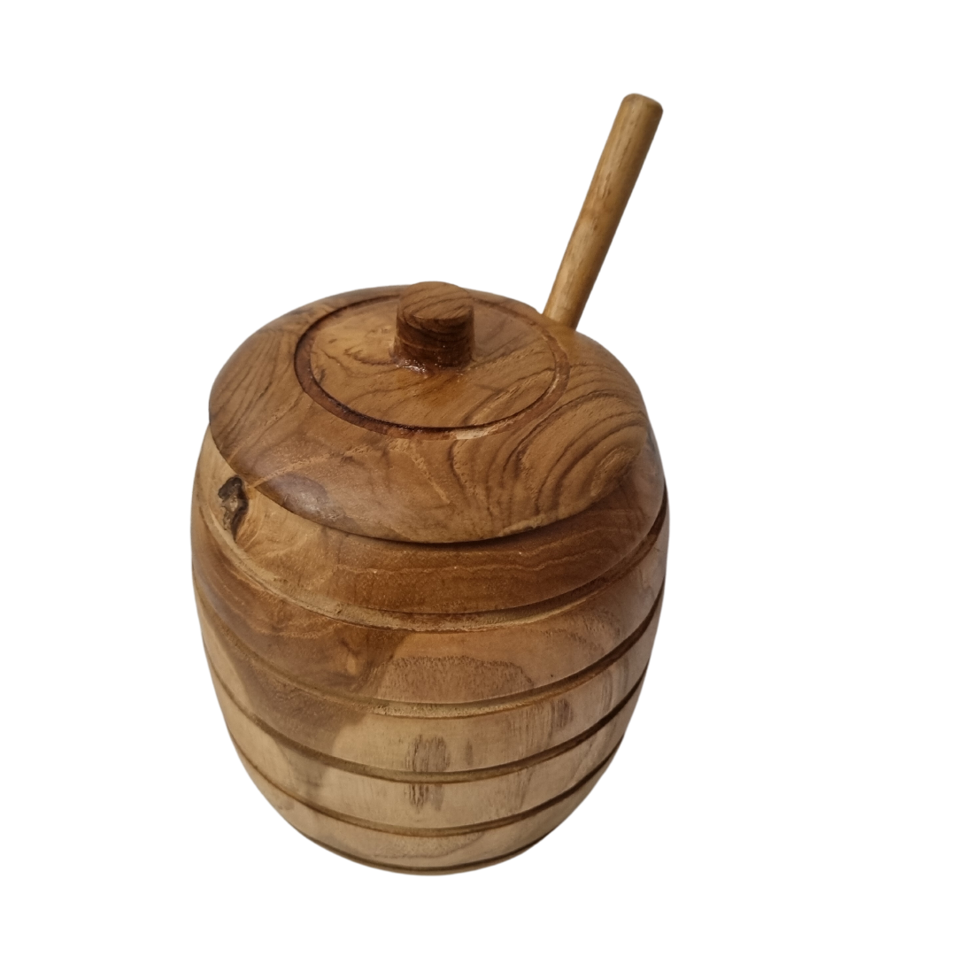 Wooden honey pot with dipper handle resting through the lid notch, showing natural grain and carved grooves.