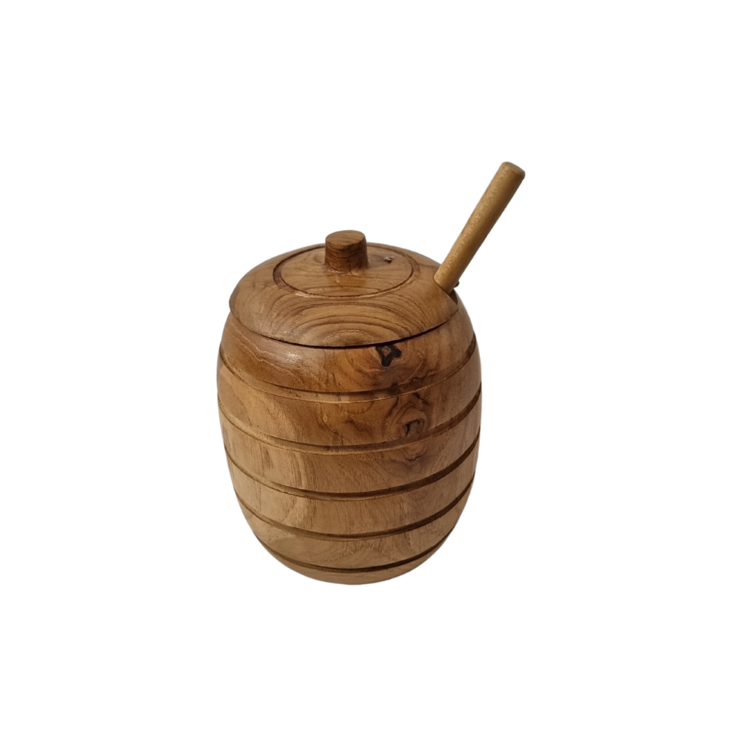 Wooden honey pot with dipper handle resting through the lid notch, showing natural grain and carved grooves.