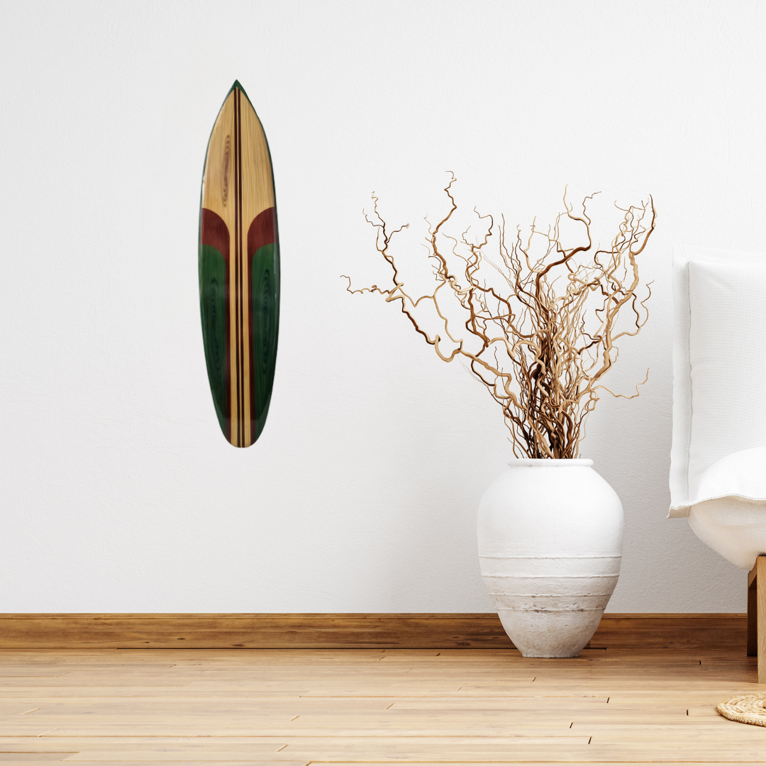 Wooden surfboard wall art in green and natural wood tones hung on a white wall beside a white textured vase with dried branches – coastal boho decor | Azure Decor