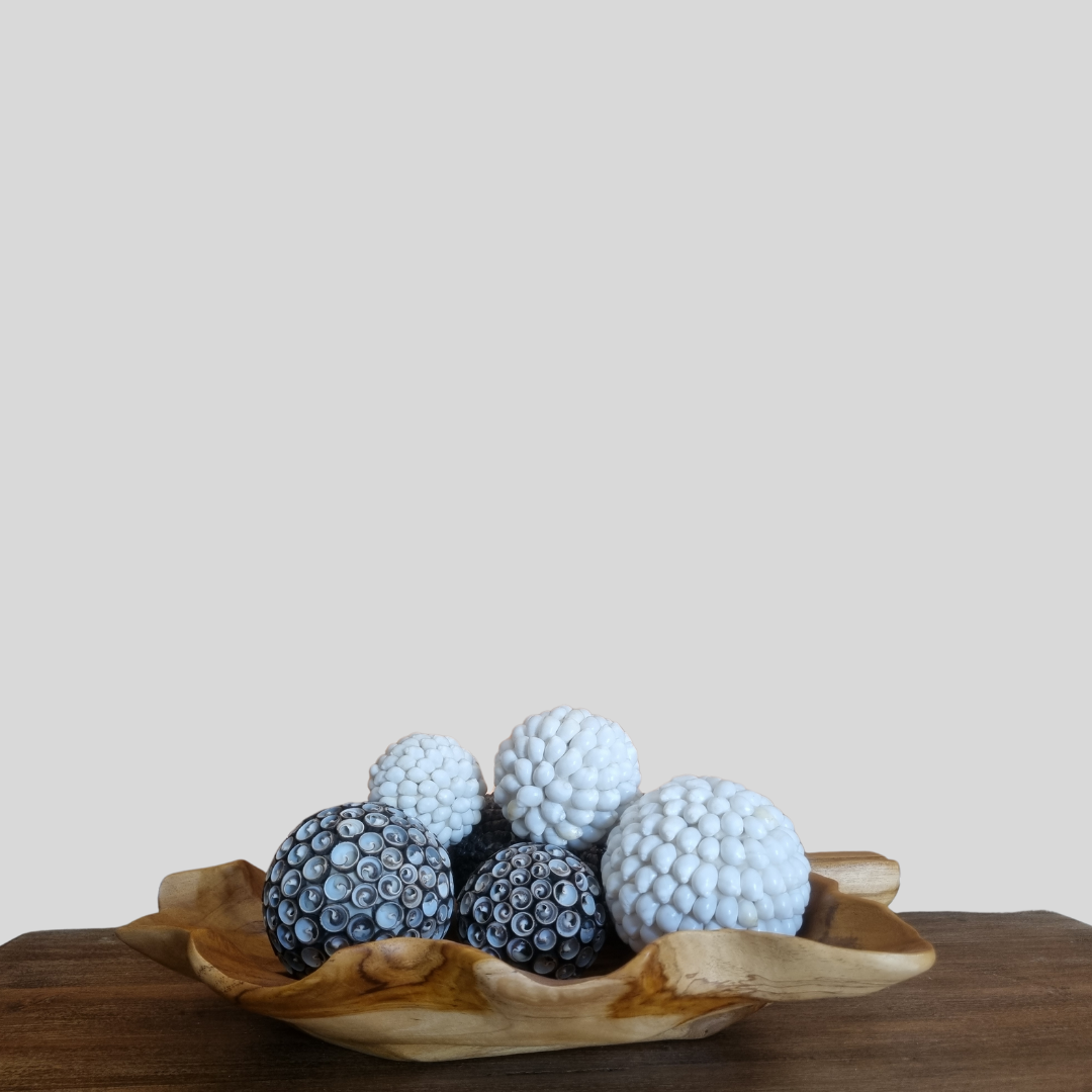 Decorative items resembling shell balls in a wooden bowl on a wooden surface with a plain background