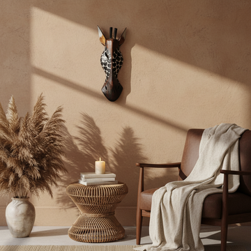 Carved wooden giraffe wall mask above a linen headboard with rattan lamp and pampas grass