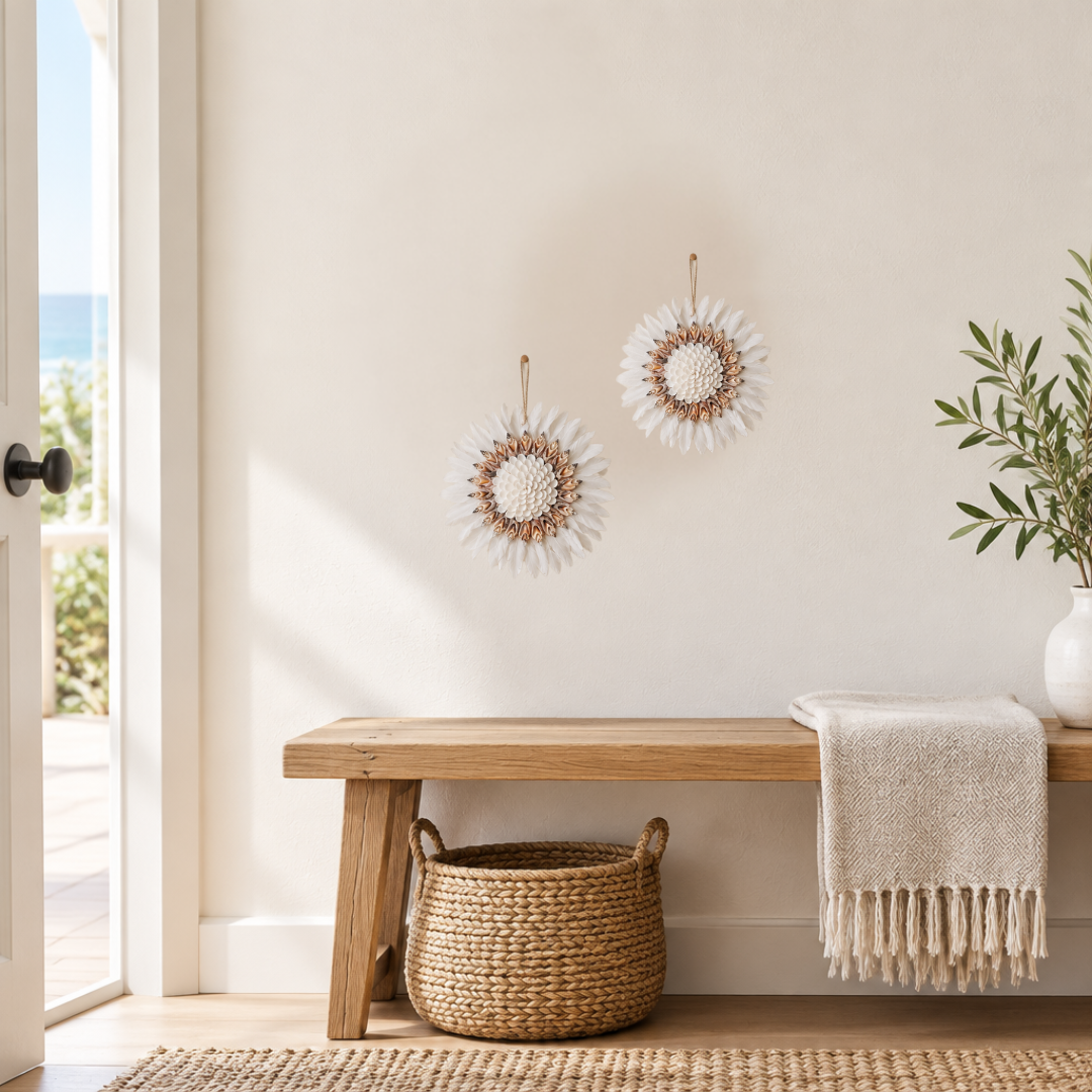 Two white feather wall hangings above a timber bench in a coastal room