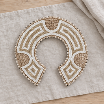 Crescent-shaped piece with beige and white beadwork laid on pale linen over a light timber surface