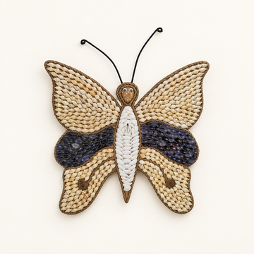 A handcrafted butterfly wall hanging made from woven or straw strips, with black wire antennae, on a plain off-white background.